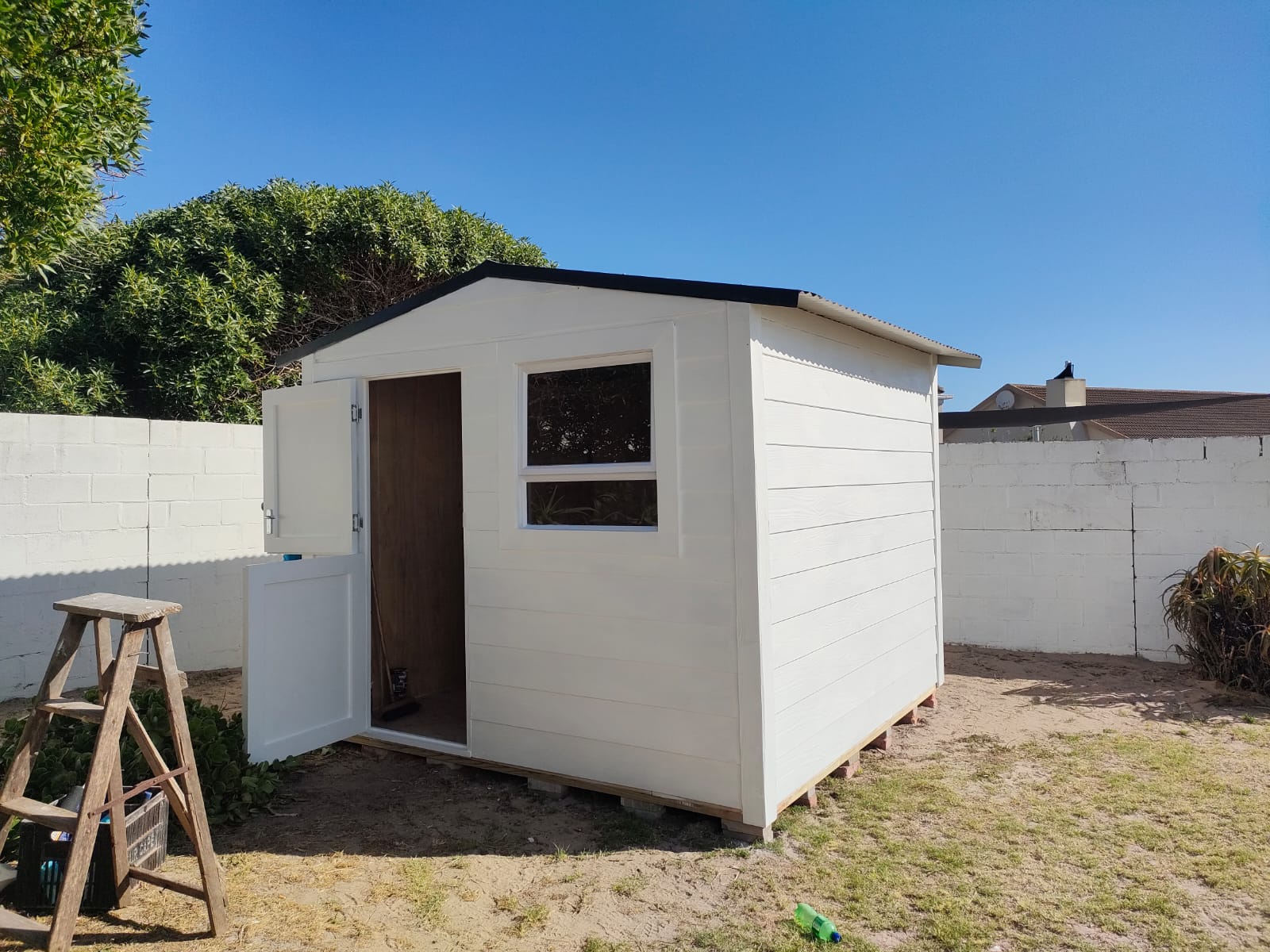 A freshly built white Wendy house with a stable door and window in a backyard