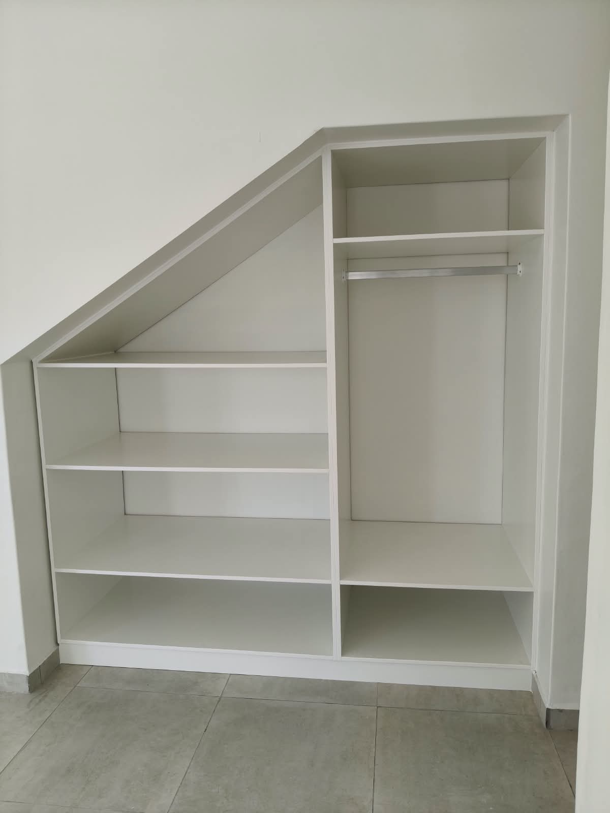 Custom built-in white shelving and cupboard unit fitted to a slanted roof